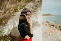 Junge brünette Frau steht in der Nähe tropischer Palmenblätter an der Küste — Stockfoto