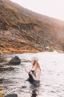 Young woman in hat and swimsuit with closed eyes meditating in water surface near rock coast — Stock Photo
