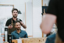 From below barber combing hair of handsome stylish male sitting in barbershop — Stock Photo