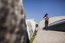 Junge brünette schlanke Frau in Sportbekleidung joggt bei sonnigem Wetter im Park — Stockfoto