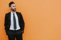 Erwachsene gut aussehende elegante Geschäftsmann in formalen Anzug Blick in die Kamera in der Nähe orangefarbene Wand — Stockfoto