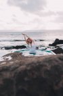 Giovane donna con gli occhi chiusi che riposa in acqua di piscina vicino a rocce e cielo nuvoloso sulla costa del mare — Foto stock