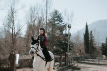 Doce menina no capacete equitação obediente cavalo branco no recinto durante a lição no dia de outono na fazenda — Fotografia de Stock