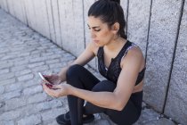 Brünette Frau sitzt und checkt Trainings-App — Stockfoto