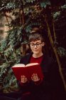 Jeune femme élégante attrayante dans le livre de lecture de lunettes et assise sur le banc dans le jardin de la ville — Photo de stock