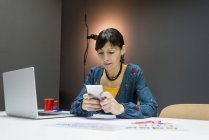 Femme d'affaires utilisant un smartphone près d'un ordinateur portable tout en travaillant dans un bureau moderne — Photo de stock