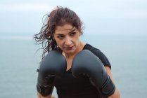 Donna adulta in abbigliamento sportivo che pratica pugni durante l'allenamento di kickboxing vicino al mare — Foto stock