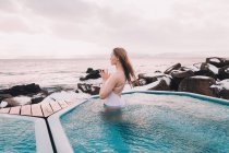 Young woman with closed eyes meditating in water of pool near rocks and cloudy sky — Stock Photo
