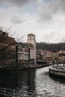 Nubes grises flotando en el cielo sobre edificios antiguos y canales con agua ondulada en un día aburrido en Bilbao, España - foto de stock