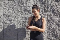 Brunette woman leaning against granite wall while using phone and laughing — Stock Photo