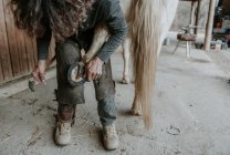 Homem adulto irreconhecível usando faca para remover a sujeira do casco de cavalo no rancho — Fotografia de Stock