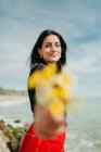 Lächelnde junge Frau, die am sonnigen Tag am Strand einen Strauß gelber Blumen überreicht — Stockfoto