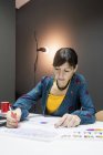 Деловая женщина в элегантном наряде делает заметки о графиках, сидя за столом в современном офисе — стоковое фото