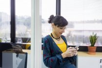 Sorridente gerente do sexo feminino usando smartphone no escritório moderno — Fotografia de Stock