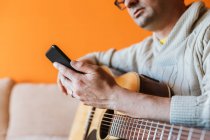 Крупный план человека с гитарой с помощью мобильного телефона — стоковое фото