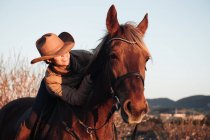 Mujer montando a caballo contra el cielo puesta del sol en rancho - foto de stock