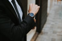 Imagen recortada del hombre de negocios en traje formal que muestra el reloj sobre fondo borroso - foto de stock
