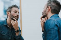 Réflexion dans le miroir de beau mâle élégant vérifiant barbe dans le salon — Photo de stock