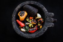 Delicious roasted vegetables in mortar on black background — Stock Photo