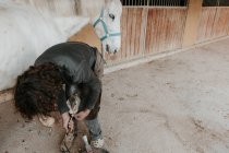 Vista lateral do ferreiro adulto usando o martelo para colocar ferradura no casco do cavalo perto do estábulo na fazenda — Fotografia de Stock