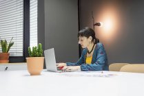 Mujer de negocios enfocada que trabaja en el ordenador portátil mientras está sentado en el escritorio en la oficina moderna - foto de stock