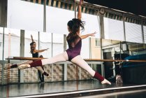 Vista trasera de la joven bailarina delgada saltando por encima del suelo en el estudio flexionando las piernas. - foto de stock