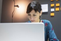 Зосереджена бізнес-леді працює на ноутбуці, сидячи за столом в сучасному офісі — стокове фото