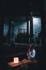 Jovem mulher com as mãos orando sentado perto de luzes no edifício escuro — Fotografia de Stock