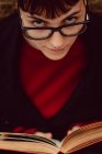 Крупный план молодой элегантной женщины в очках с книгой, смотрящей в камеру — стоковое фото