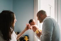 Дорослий чоловік і жінка ніжно торкаються і розмовляють з чарівною новонародженою дитиною в затишному дитячому будинку — стокове фото