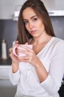 Portrait of young woman holding mug in modern kitchen at home — Stock Photo