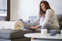 Весела молода жінка використовує ноутбук і відпочиває на дивані вдома — стокове фото