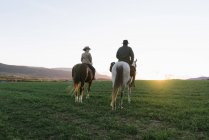Rückansicht von Mann und Frau, die auf einer Ranch Pferde gegen den Sonnenuntergang reiten — Stockfoto