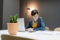 Деловая женщина, работающая с документами, сидя за столом с ноутбуком в современном офисе — стоковое фото