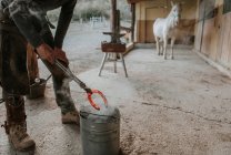 Erwachsener Hufschmied schmiedet mit Hammer und Zange heißes Hufeisen auf tragbarem Amboss in der Nähe des Stalls auf der Ranch — Stockfoto