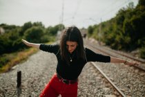 Cheerful young woman in stylish outfit having fun while standing on blurred background of rails — Stock Photo