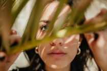 Крупним планом чуттєва молода жінка дивиться через зелений лист тропічної долоні — стокове фото
