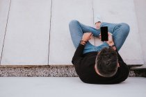 Гарний елегантний щасливий чоловік у повсякденному одязі, використовуючи мобільний телефон і сидячи біля сірої стіни — стокове фото
