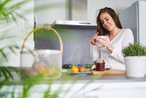 Молода усміхнена жінка тримає кухоль і сніданок на сучасній кухні вдома — стокове фото
