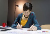 Empresária fazendo anotações de gráficos enquanto se senta na mesa no escritório moderno — Fotografia de Stock