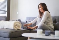 Весела молода жінка використовує ноутбук і відпочиває на дивані вдома — стокове фото