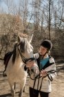 Женщина ухаживает за лошадью возле конюшни после урока в солнечный день на ранчо — стоковое фото
