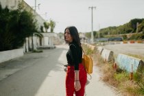Allegro giovane donna in abito alla moda guardando la fotocamera mentre cammina su sfondo sfocato di parcheggio in campagna — Foto stock