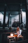 Giovane donna seduta vicino alle luci in un edificio buio — Foto stock