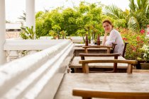 Улыбающаяся женщина в кафе на открытом воздухе возле тропических растений — стоковое фото