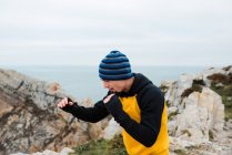 Homme barbu adulte en vêtements de sport pratiquant des coups de poing pendant l'entraînement de kickboxing sur une falaise rocheuse près de la mer — Photo de stock