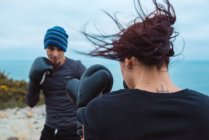 Homme et femme en gants de boxe se frappant mutuellement tout en se tenant sur la côte de la mer — Photo de stock