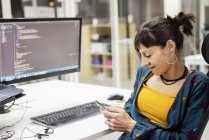 Жіночий менеджер використовує смартфон біля екрану комп'ютера під час роботи в сучасному офісі — стокове фото
