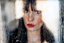 Mulher atraente com lábios vermelhos beijando atrás de vidro transparente — Fotografia de Stock