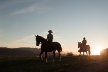 Uomo e donna a cavallo contro il cielo al tramonto nel ranch — Foto stock